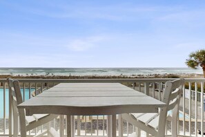 En balkon med et bord og stole med udsigt over en strand og hav.