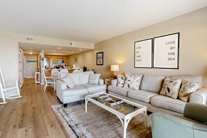 A modern living room with a sofa, a coffee table, and a dining area in the background. - Dreamy Beach Gem W/ Shared Pool, Private Balcony, Water Views & Fast WiFi (Pensacola Beach)