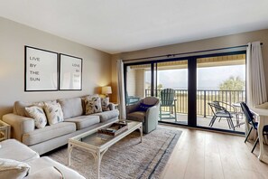 A living room with a sofa, coffee table, and a view of the sea through a sliding glass door. - Dreamy Beach Gem W/ Shared Pool, Private Balcony, Water Views & Fast WiFi (Pensacola Beach)