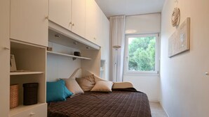 A bedroom with a bed, built-in wardrobe, and a window with a view of greenery. - Villa Oliva 8 - Carraro Immobiliare Jesolo (Lido di Jesolo)
