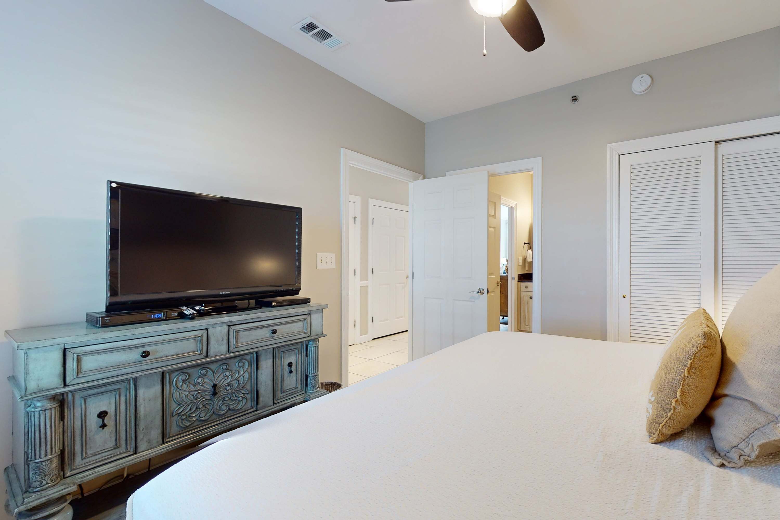 A bedroom with a bed, a television on a dresser, and a closet with louvered doors.