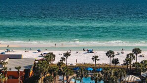 A beach with clear blue water, white sand, and palm trees. There are umbrellas and people on the beach. - Oceanfront 10th-floor condo with great view, balcony, WiFi, AC, & WD (Destin)