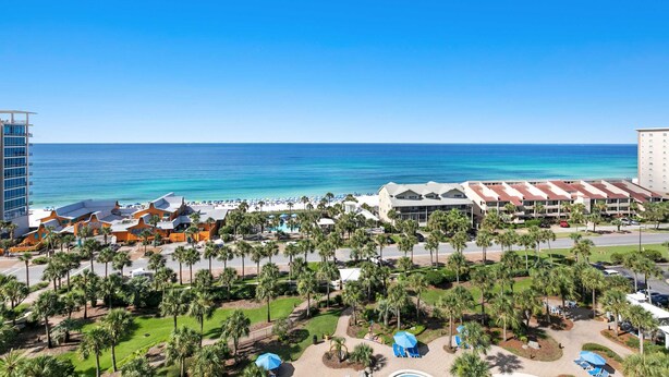 A resort with a pool area, palm trees, and a view of the ocean. - Oceanfront 10th-floor condo with great view, balcony, WiFi, AC, & WD (Destin)