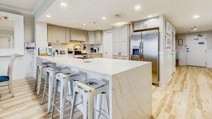 A modern kitchen with a large island, bar stools, and a stainless steel refrigerator. - Oceanfront 10th-floor condo with great view, balcony, WiFi, AC, & WD (Destin)