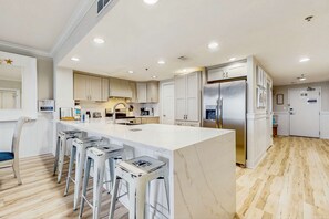 A modern kitchen with a large island, bar stools, and a stainless steel refrigerator. - Oceanfront 10th-floor condo with great view, balcony, WiFi, AC, & WD (Destin)