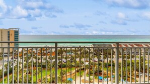 A balcony with a view of a beach and ocean, surrounded by palm trees and buildings. - Oceanfront 10th-floor condo with great view, balcony, WiFi, AC, & WD (Destin)