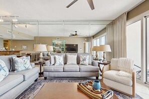 Un salon moderne avec un canapé gris, des fauteuils, une table basse et un téléviseur.