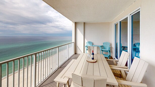 A balcony with a view of the ocean, a table with chairs, and a bottle of wine. - Oceanfront condo with scenic balcony, resort amenities, central AC, & W/D (Panama City Beach)