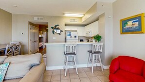 A compact living space with a kitchenette, a dining area, and a red chair. - Colorful oceanfront condo with Gulf views, on-site pools & hot tub (Panama City Beach)