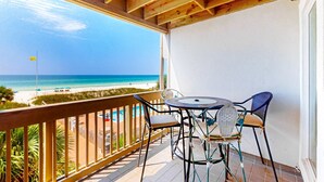 Een balkon met uitzicht op het strand, een tafel met stoelen en een houten plafond.