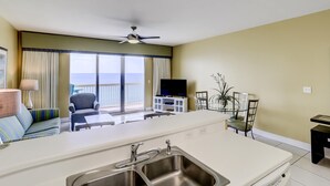 A modern hotel room with a large balcony, a TV, a dining area, and a kitchen with a sink. - Oceanfront condo w/ shared pools, hot tub, tennis courts - walk to the beach (Panama City Beach)