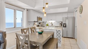 Una cocina moderna con armarios blancos, un refrigerador de acero inoxidable y un comedor con mesa y sillas de madera.