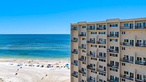 Un hotel frente a la playa con varios balcones, una playa de arena y un cielo azul despejado.