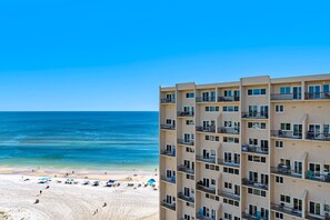 A beachfront hotel with multiple balconies, a sandy beach, and a clear blue sky. - Oceanfront penthouse with pools, sauna, beach access & breathtaking ocean views (Panama City Beach)