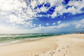 A beach with footprints leading to the water, a clear sky, and a distant shoreline. - Pretty snowbird condo w lake views, free WiFi, and full kitchen (Panama City Beach)