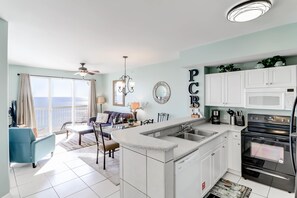 Una cocina moderna con armarios blancos, una isla integrada y un amplio ventanal con vistas al océano.