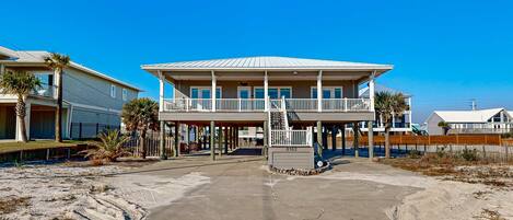 A beachfront house with a balcony, a covered porch, and a sandy driveway.