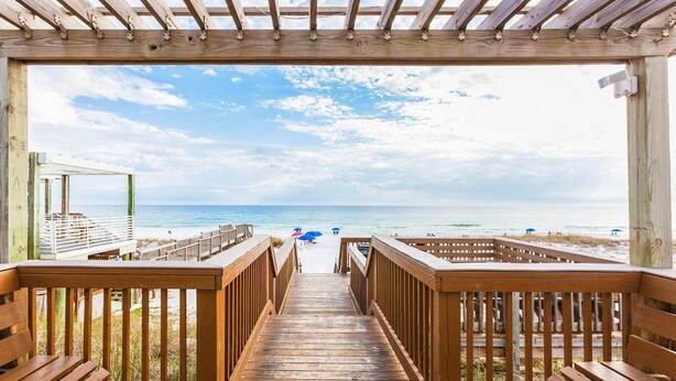 Une terrasse en bois qui mène à une plage, sous un ciel dégagé.