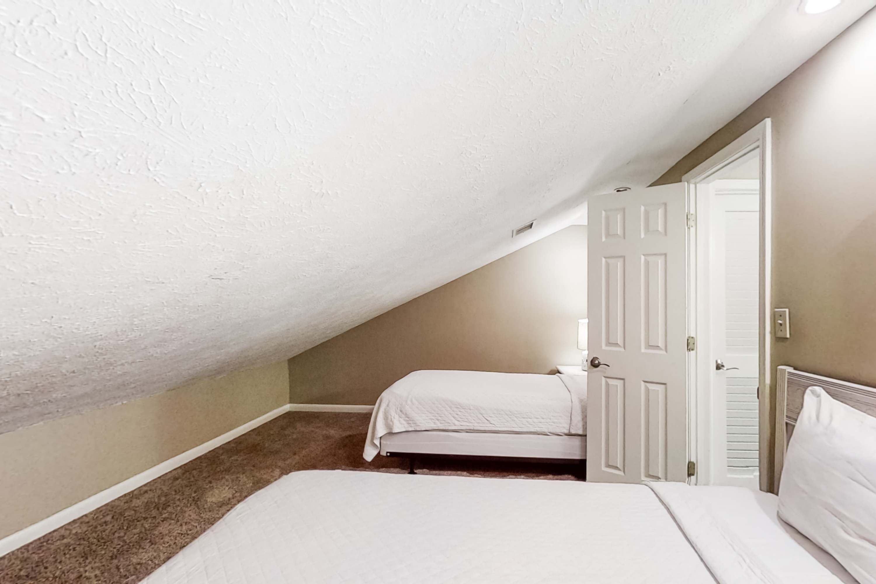 Une chambre avec deux lits, un plafond en pente et une porte.