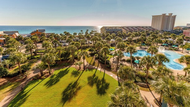 Um resort com piscina, palmeiras e vista para o mar.