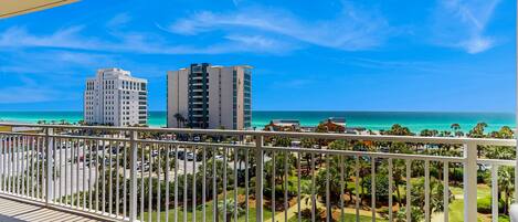 A balcony with a view of a beach, palm trees, and buildings.