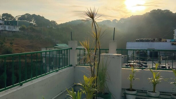Una terraza en la azotea con plantas en macetas, baranda verde y vista del atardecer sobre un paisaje montañoso.