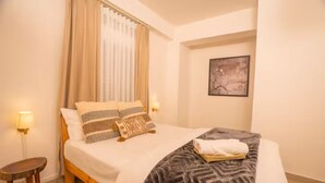 Una cama bien hecha con ropa de cama estampada, una mesita de noche y una lámpara de pared.