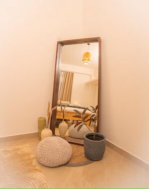 Une pièce avec un grand miroir, un lit, une plante en pot et un pouf rond.