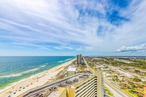 A coastal hotel with a beach view, multiple parking levels, and a prominent building in the background. - 2nd Floor Cute Gulf Front Condo Many Amenities, Private Beach Access (Navarre Beach)