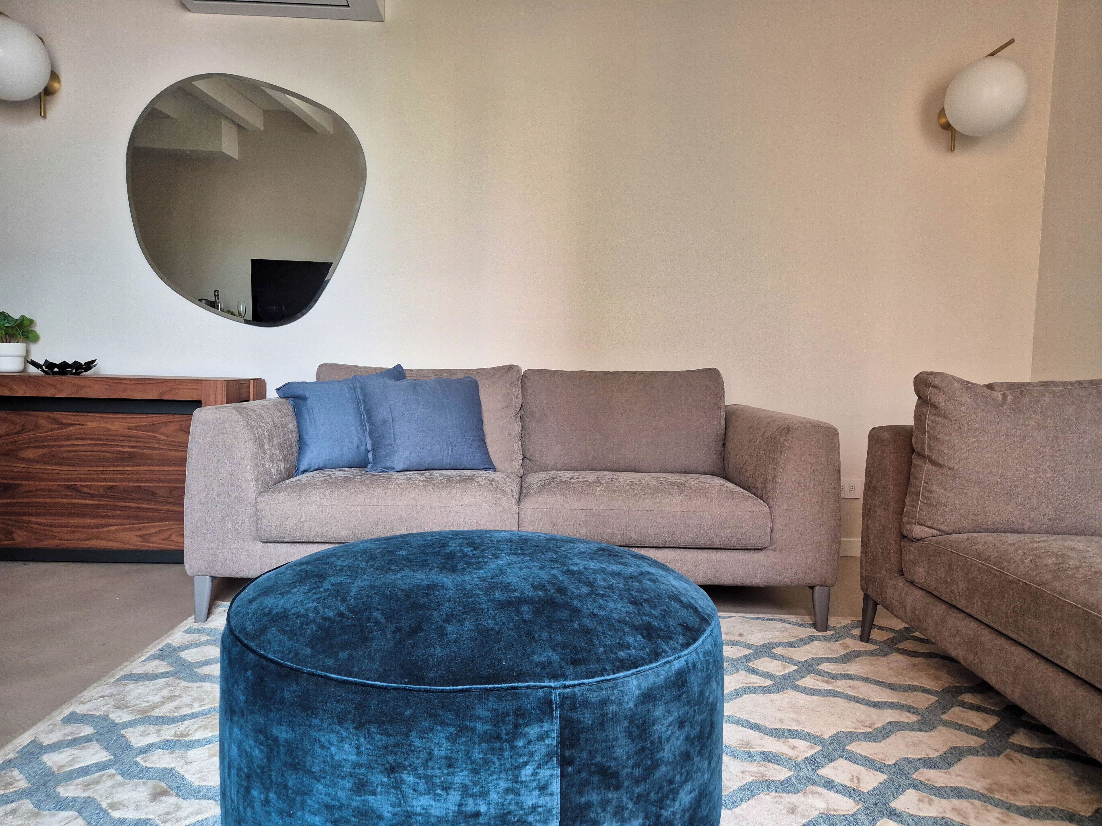 Ein Wohnzimmer mit rundem Hocker, einer Couch und einem Spiegel an der Wand.