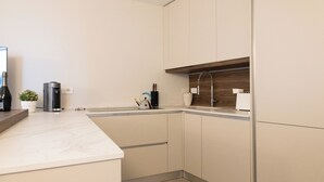Eine moderne Küche mit Marmorarbeitsplatte, integrierten Schränken und einem Holzregal.