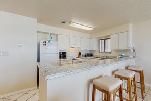 A modern kitchen with white cabinets, a marble countertop, and a built-in island with bar stools. - Gorgeous, Open Ground Floor Condo Gulf Front w Large Patio &  Beach Access (Destin)
