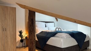 Een moderne slaapkamer met een houten garderobe, een nachtkastje met lamp, een bed met een hartvormige kussenset, en een schuine plafond.