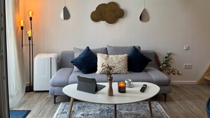 Een moderne woonkamer met een grijze bank, een ronde salontafel, een laptop, een kaars en een afstandsbediening.