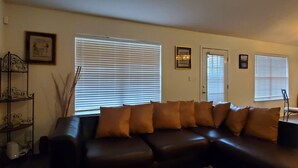 A living room with a dark leather sofa, multiple windows with blinds, a door, and a framed picture on the wall. - Private home near the beach with washer and dryer and free Wifi (Navarre)