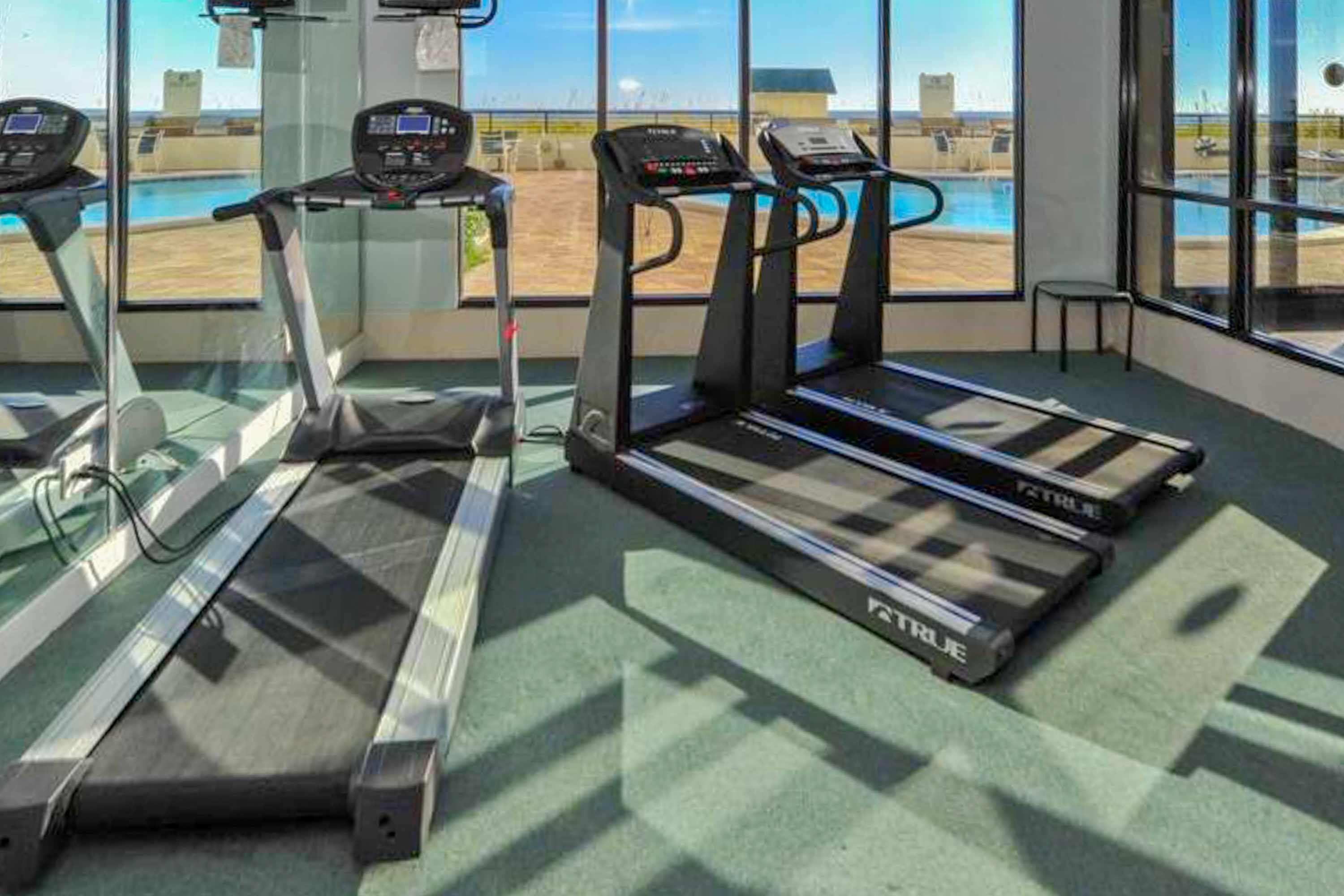 A gym with treadmills and a view of a pool through large windows.