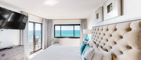 Ein Hotelzimmer mit einem großen Bett, einem Flachbildfernseher, einem Schminktisch und Blick aufs Meer.