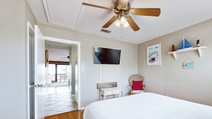 Ein Schlafzimmer mit Bett, Deckenventilator, Fernseher, Sessel und kleinem Tisch.