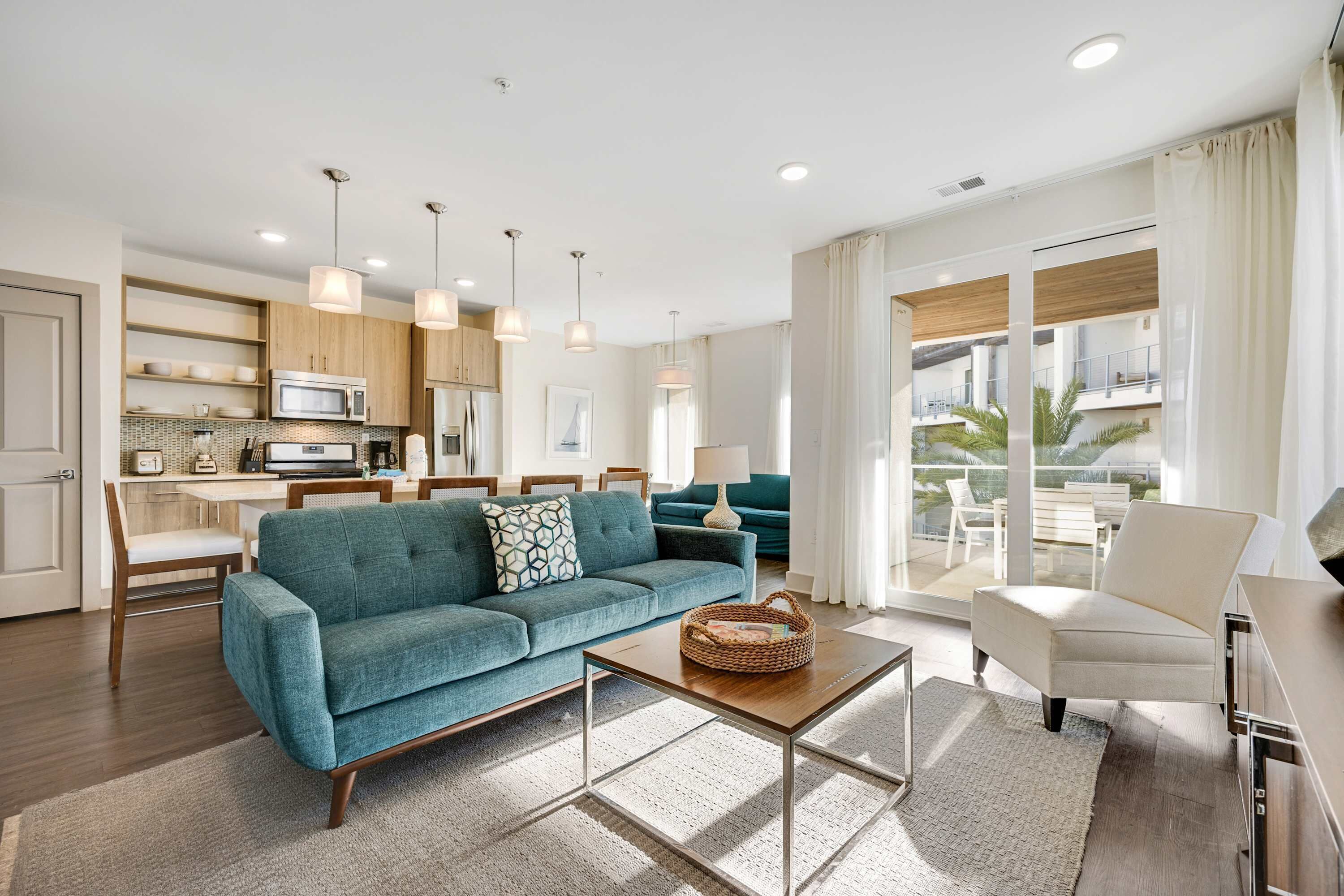 A modern living room with a teal sofa, a wooden coffee table, and a dining area with a white table and chairs.