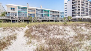 A beachfront hotel with multiple balconies, a sandy beach in the foreground, and a clear blue sky. - Beachfront townhome with large deck & Gulf view - near Pier Park (Panama City Beach)