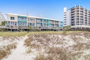 A beachfront hotel with multiple balconies, a sandy beach in the foreground, and a clear blue sky. - Beachfront townhome with large deck & Gulf view - near Pier Park (Panama City Beach)