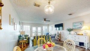 A spacious living room with a dining area, large windows, a ceiling fan, and a wall-mounted TV. - Beachfront townhome with large deck & Gulf view - near Pier Park (Panama City Beach)