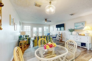 A spacious living room with a dining area, large windows, a ceiling fan, and a wall-mounted TV. - Beachfront townhome with large deck & Gulf view - near Pier Park (Panama City Beach)