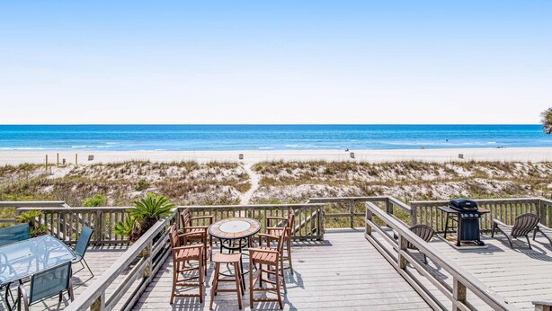 A wooden deck with a table and chairs overlooking a beach. - Beachfront townhome with large deck & Gulf view - near Pier Park (Panama City Beach)
