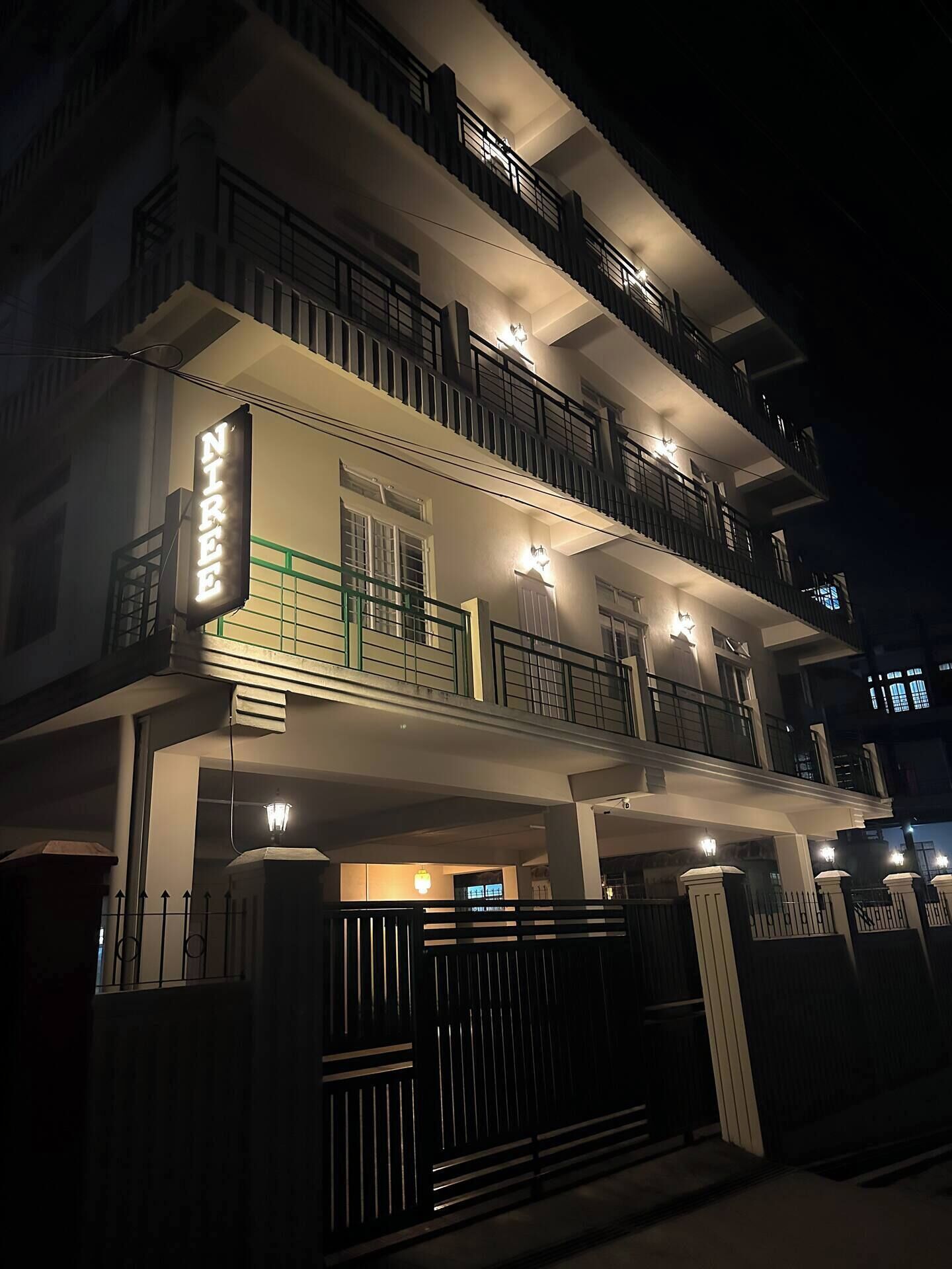 A multi-story residential building with balconies, a gated entrance, and illuminated signage.
