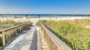 Een houten looppad dat naar een strand leidt, met parasols en ligstoelen.
