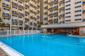 Una piscina con cerca blanca, rodeada por un edificio de varios pisos con balcones.