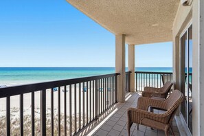 Un balcón con sillones de mimbre, vista a la playa y cielo despejado.