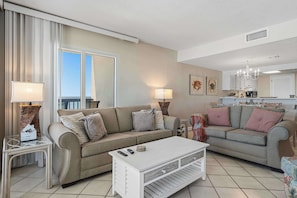 A living room with two sofas, a coffee table, and a dining area with a table and chairs. - Beachfront condo with furnished balcony, pools, tennis courts, & hot tub (Panama City Beach)