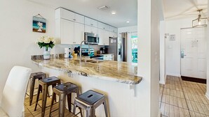 Una cocina moderna con armarios blancos, encimera de mármol y electrodomésticos de acero inoxidable. Hay cuatro taburetes y un jarrón con flores en la encimera.